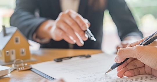 two people signing a contract with house figurine